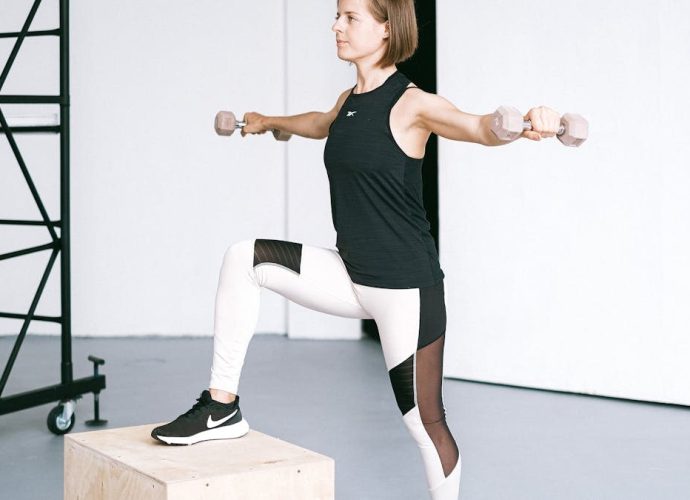 Woman performing fitness exercise with dumbbells in a gym setting, showcasing strength and balance.